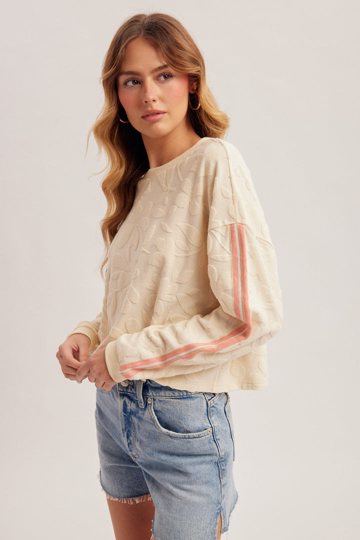 Woman wearing a beige sweater with pink stripes and denim shorts on a white background