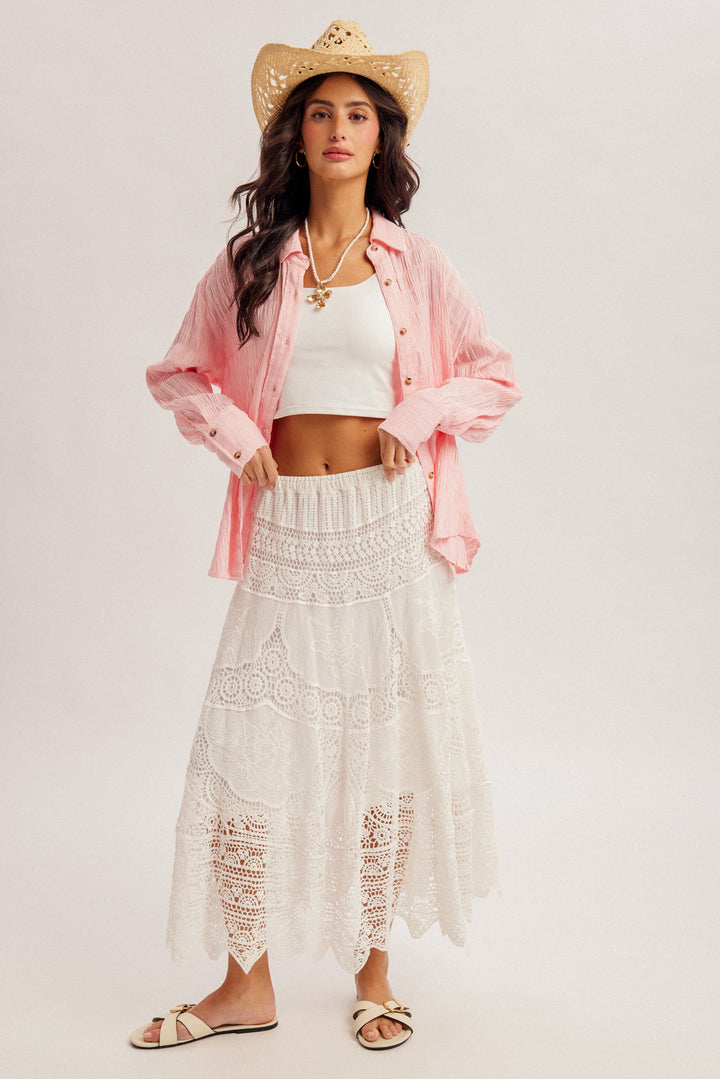 Woman wearing a pink shirt, white top, and white lace pants with a straw hat on a light background