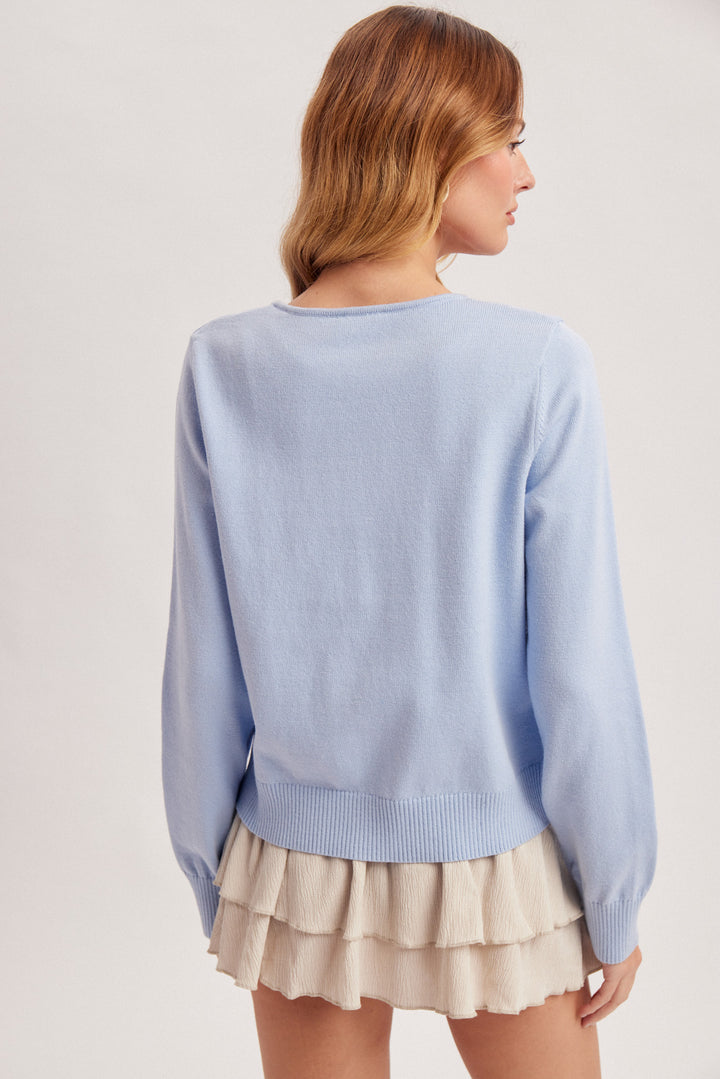 Woman wearing a light blue sweater and beige skirt on a plain background