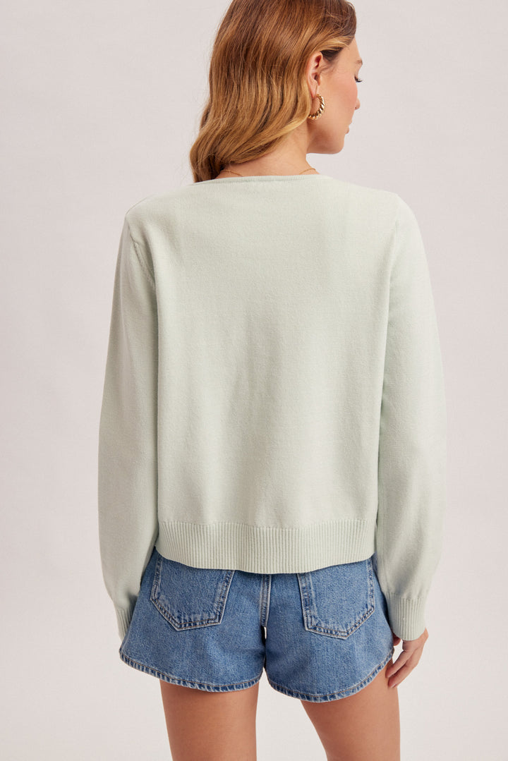 Person wearing a light green sweater and denim shorts on a plain background