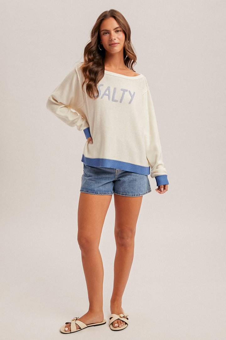 Woman wearing a white sweatshirt with blue accents and denim shorts on a plain background