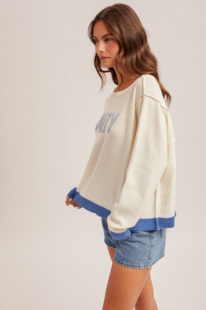 Woman wearing a cream sweatshirt with blue trim and denim shorts on a plain background