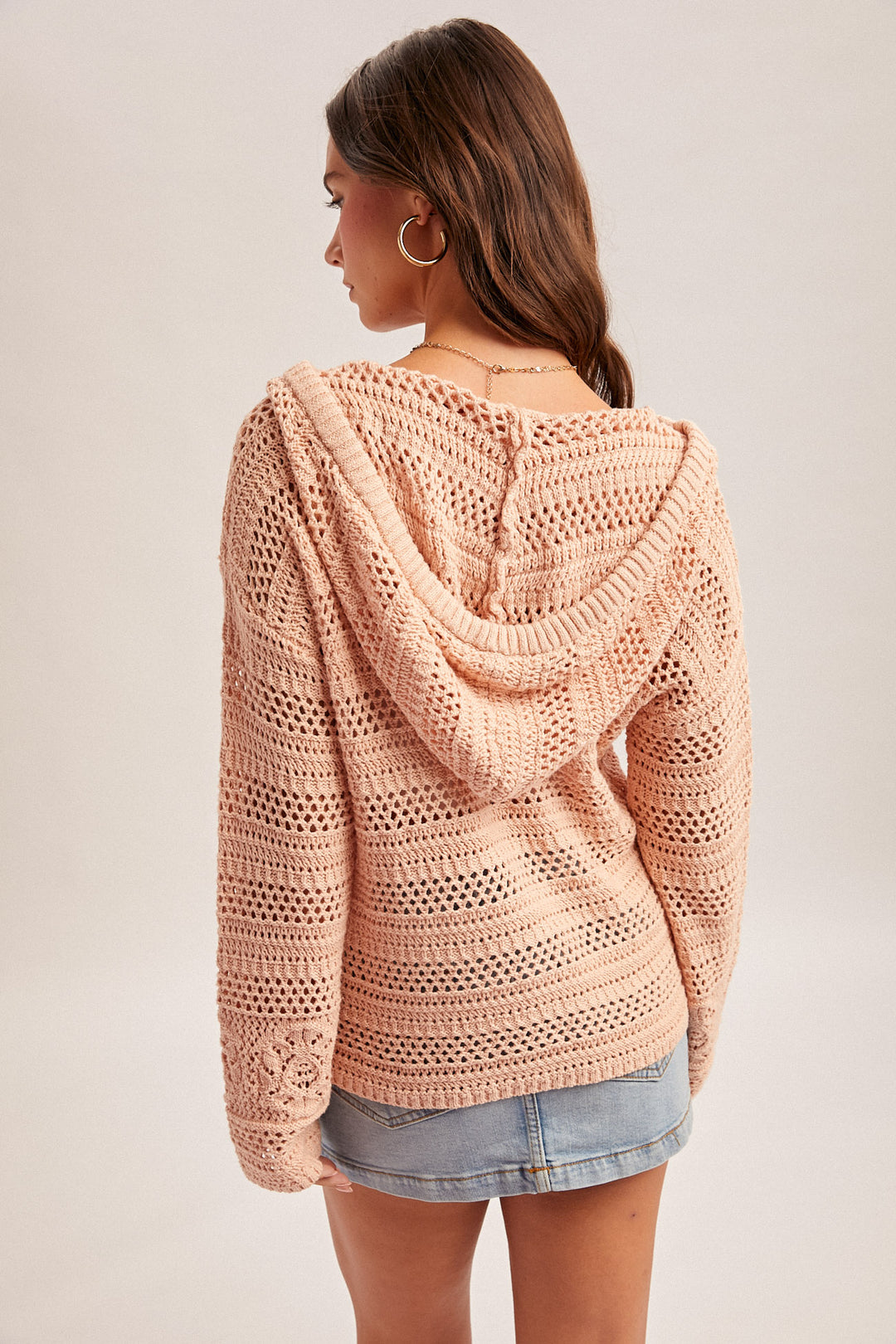 Woman wearing a pink crochet hoodie against a neutral background