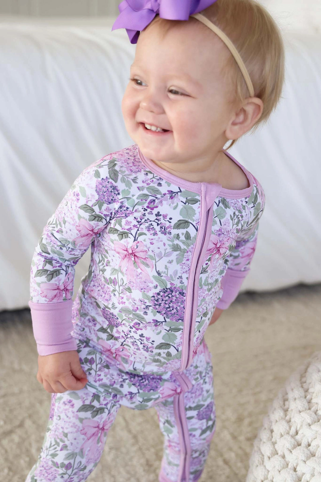 Baby in a floral onesie with a purple bow on a white background