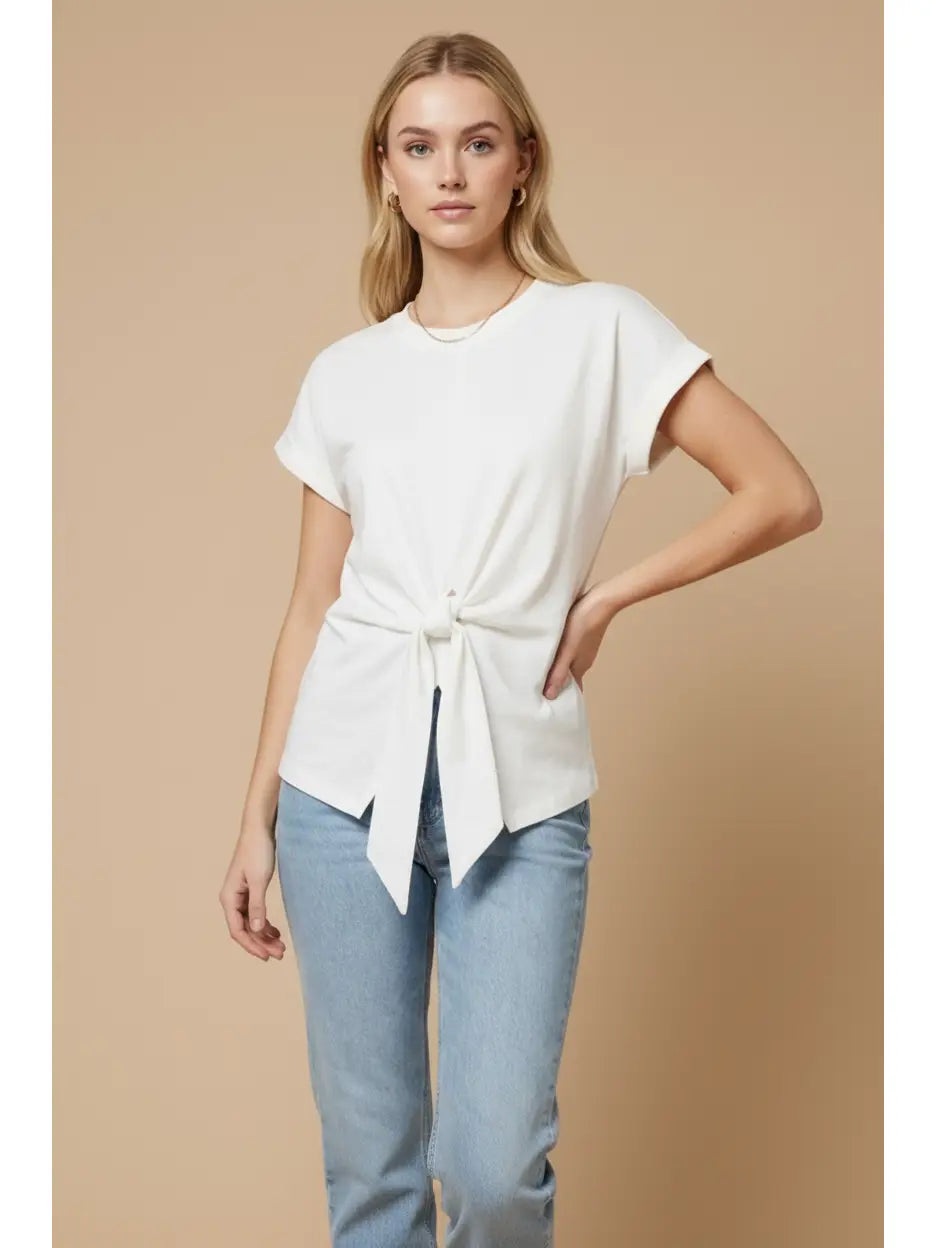 Woman wearing a white tie-front top and light blue jeans on a beige background