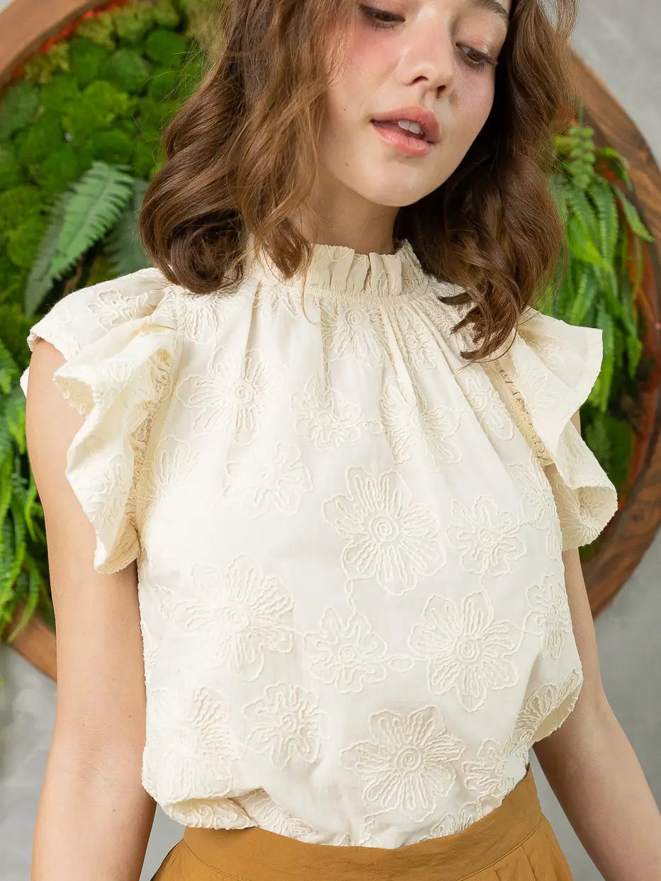 Woman wearing a white blouse with ruffled sleeves in front of green plants