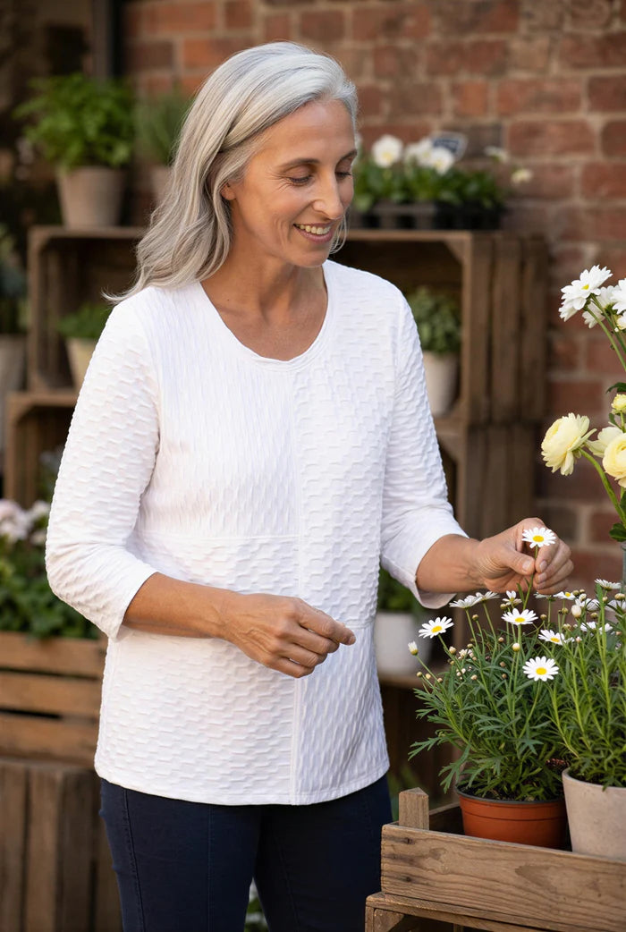Woman in a white sweater interacting with flowers in an outdoor setting