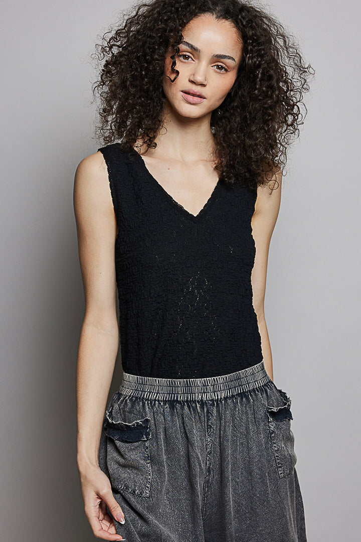 Woman wearing a black sleeveless top and gray pants against a plain background