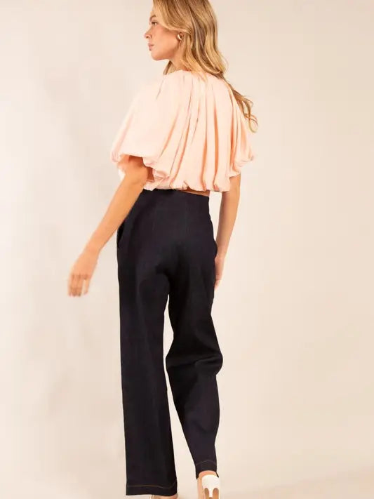 Woman wearing a pink top and black pants against a beige background