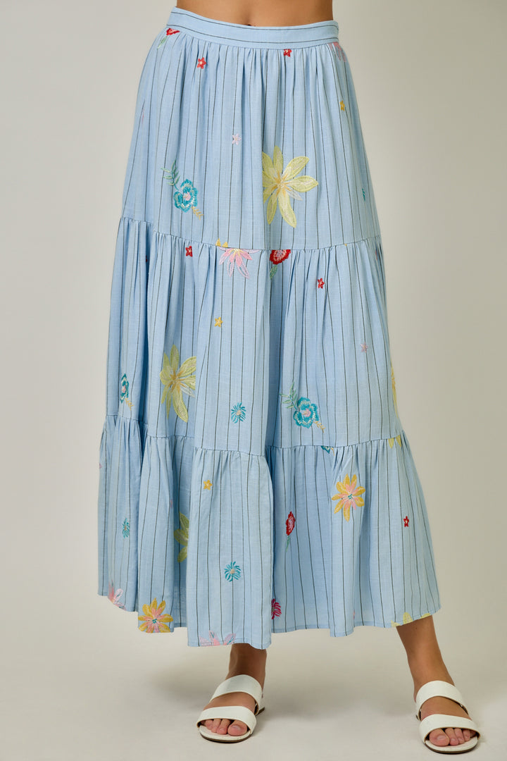Light blue tiered skirt with floral embroidery on a neutral background