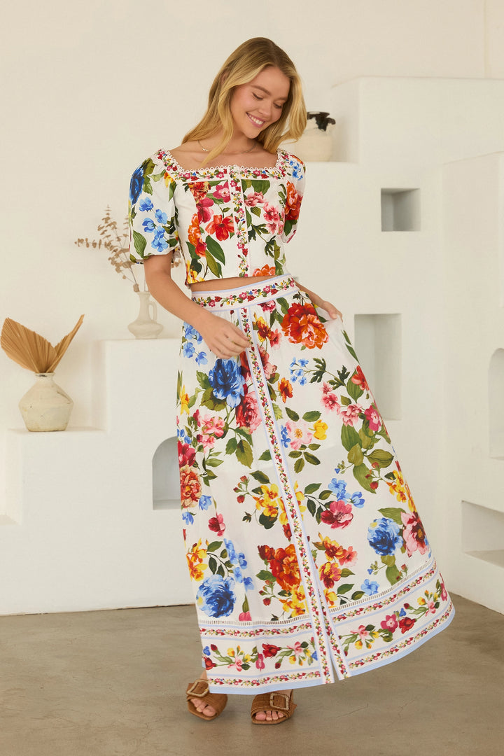 Woman wearing a colorful floral outfit standing in a minimalistic room.