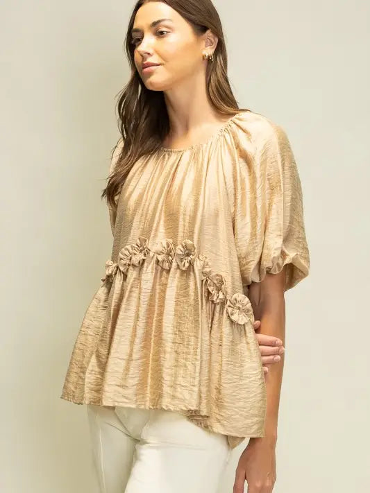 Woman wearing a beige blouse with floral details against a plain background