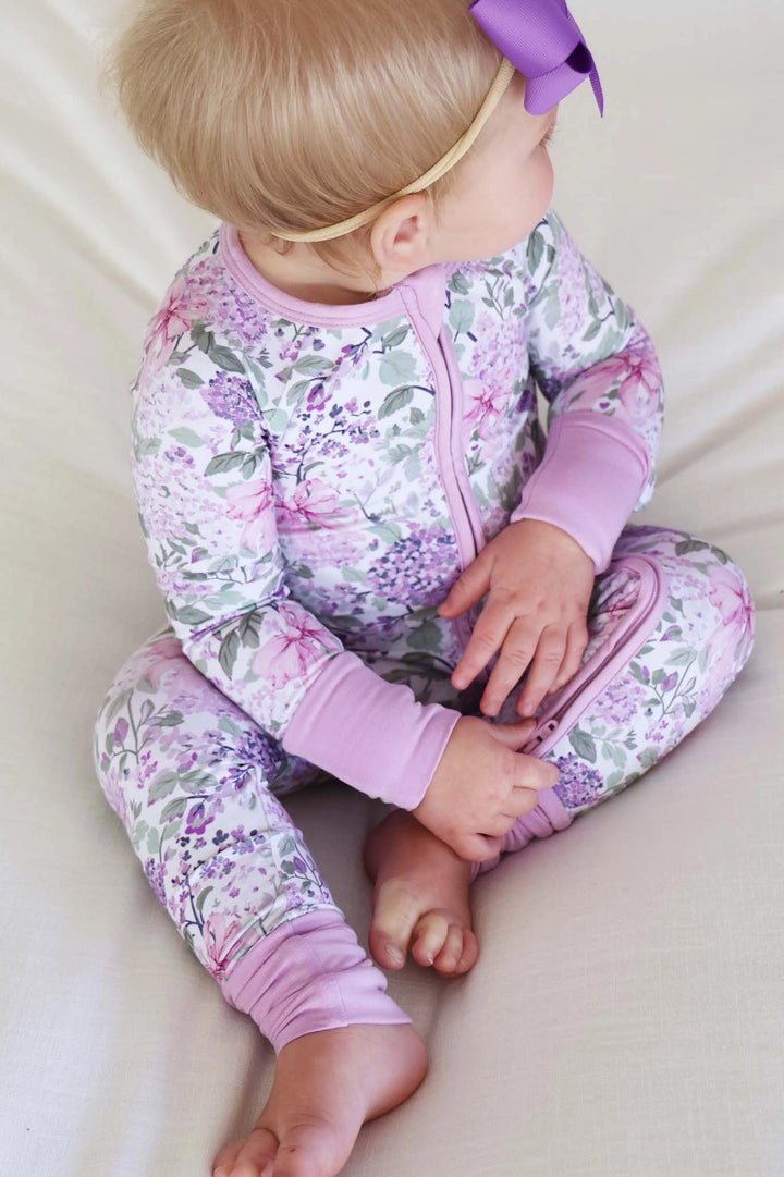 Baby in floral pajamas with a purple bow on a light background