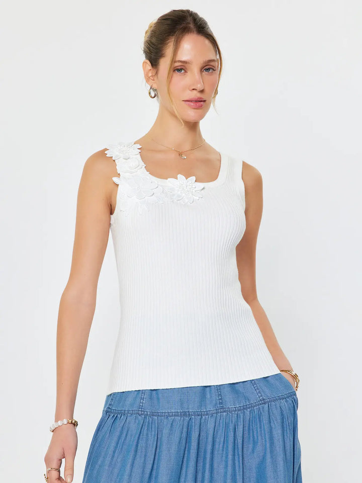Woman wearing a white sleeveless top with floral details and a blue skirt on a light gray background