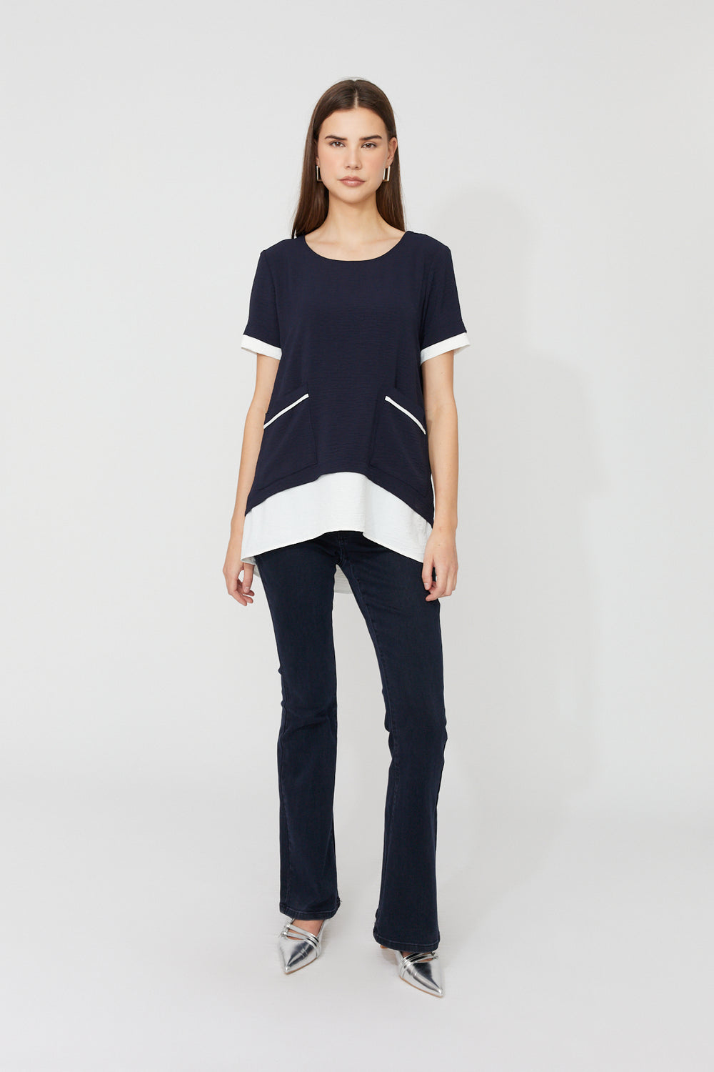 Woman wearing a black and white top with dark jeans on a light gray background