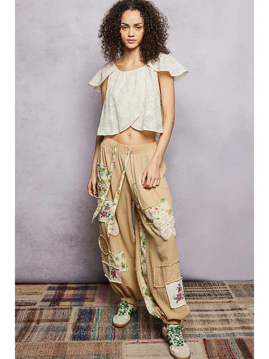 Woman wearing a light-colored top and beige pants with floral patterns against a plain background