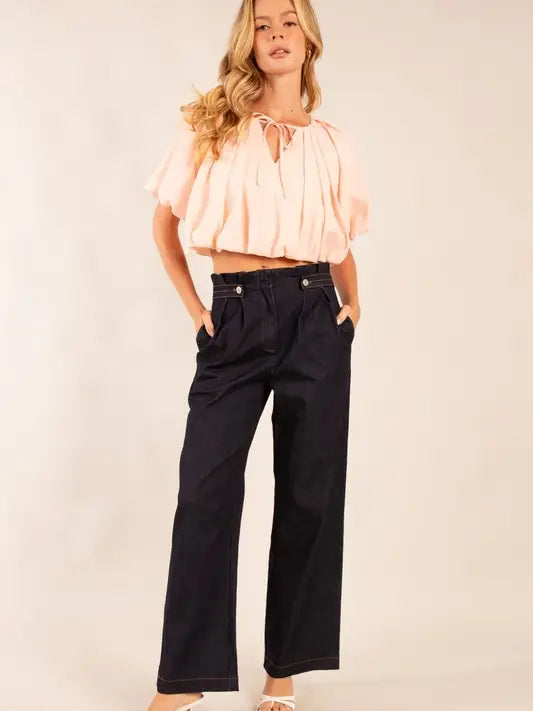 Woman wearing a light pink blouse and black pants on a plain background