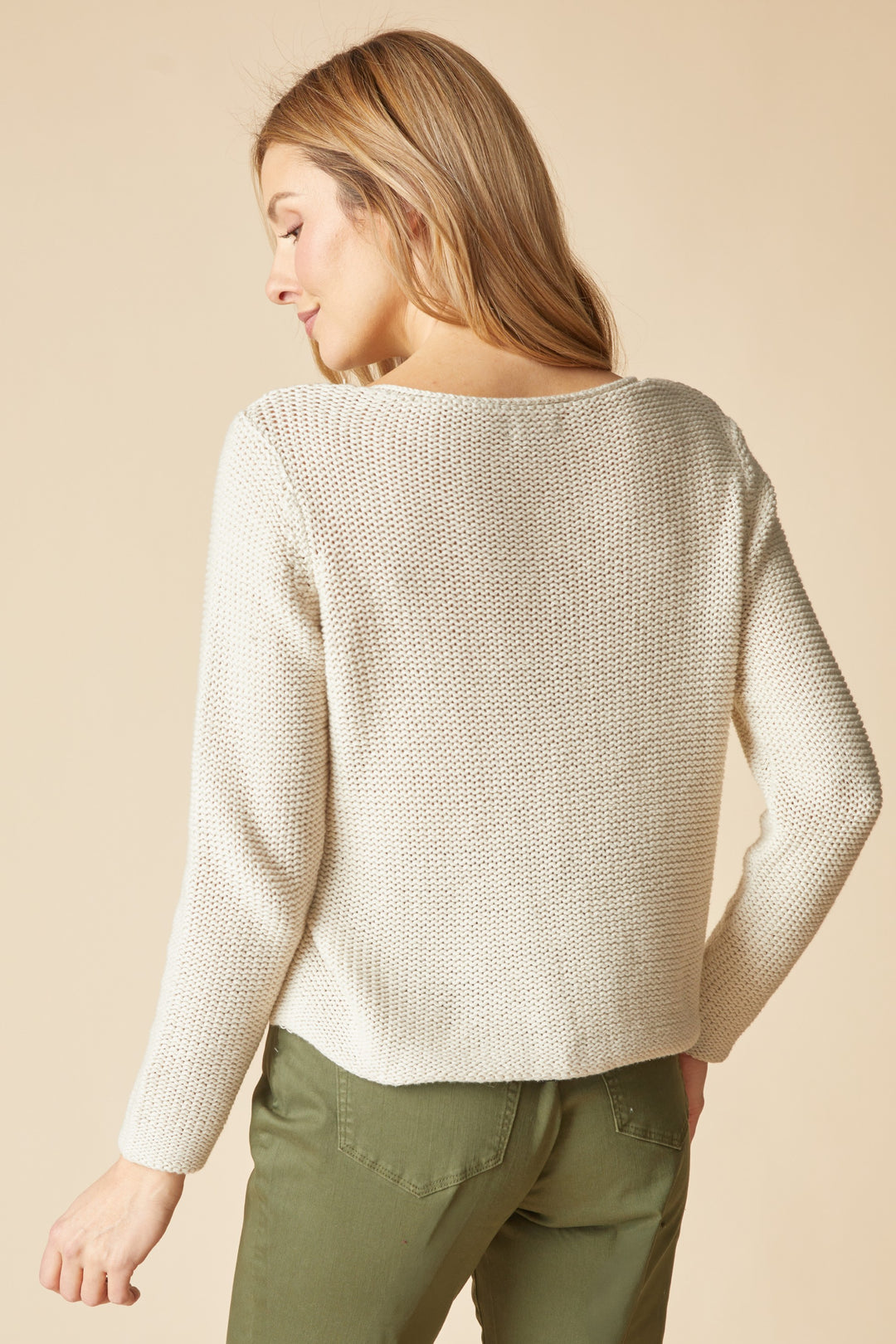 Woman wearing a beige sweater and green pants against a beige background
