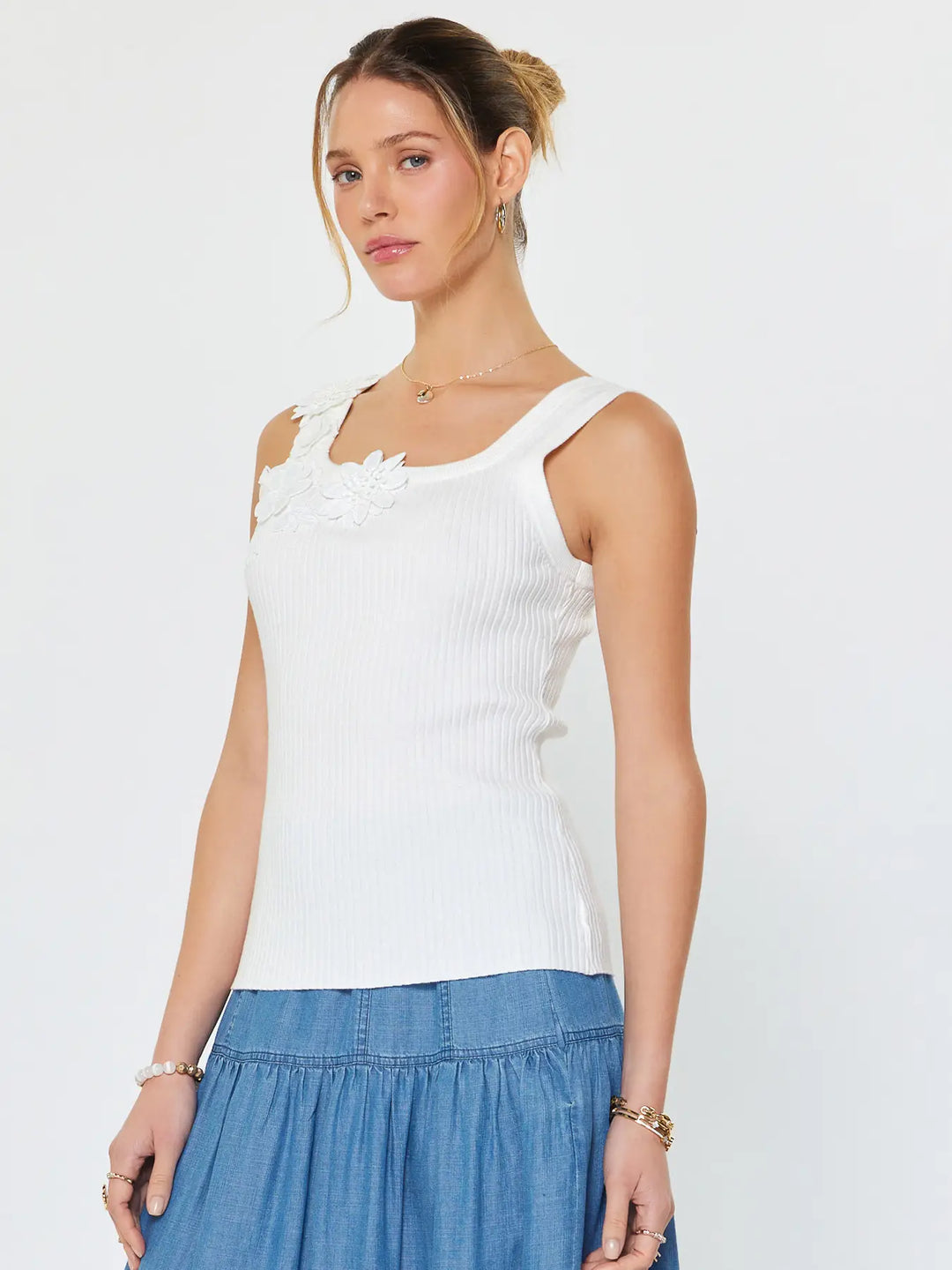 Woman wearing a white sleeveless top with floral details and a blue skirt on a light gray background