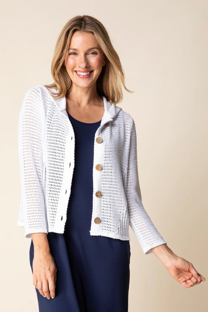 Woman wearing a white textured cardigan over a navy dress on a beige background