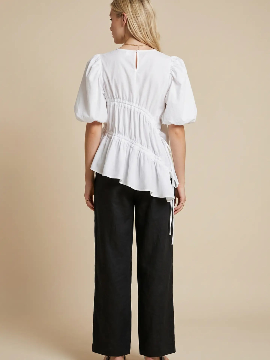 Woman wearing a white blouse with puffed sleeves and black pants on a beige background