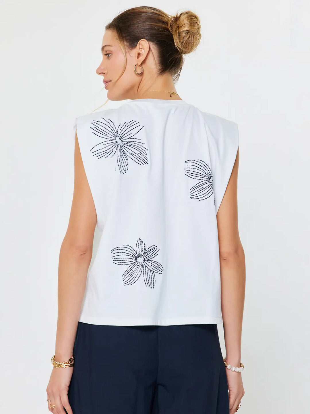 Woman wearing a white sleeveless top with black floral patterns on a plain background