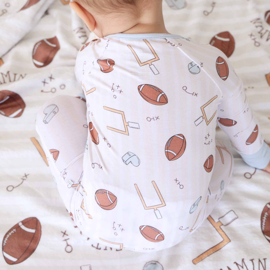 Baby wearing a onesie with sports-themed pattern on a matching blanket