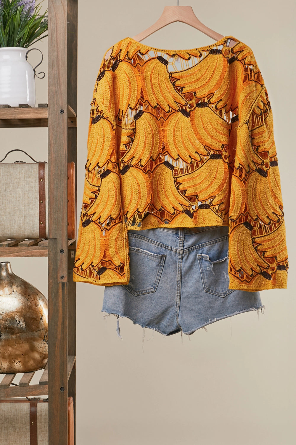 Yellow banana print top with denim shorts on a hanger against a neutral wall.