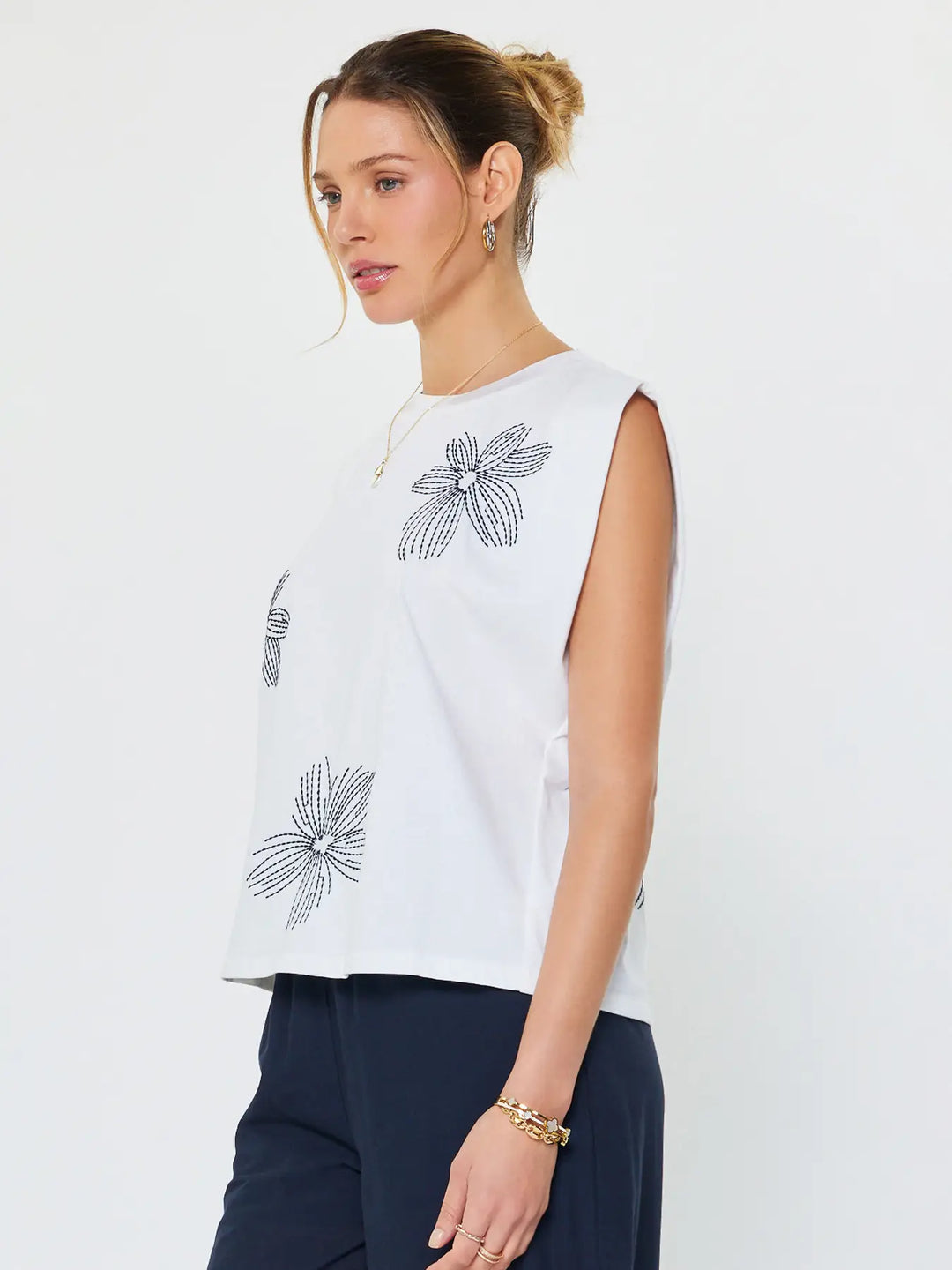 Woman wearing a white sleeveless top with black floral patterns on a plain background