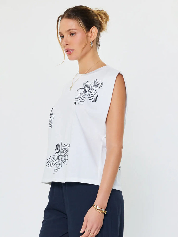 Woman wearing a white sleeveless top with black floral patterns on a plain background