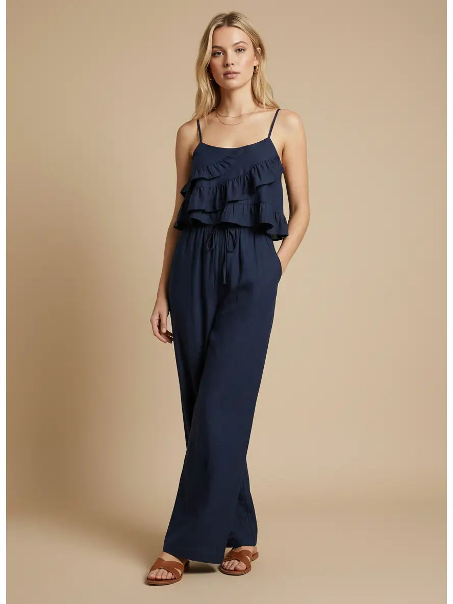 Woman wearing a navy blue jumpsuit with ruffled top on a beige background