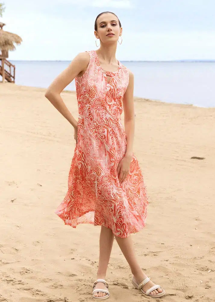 Woman in a orange and white patterned dress standing on a sandy beach.