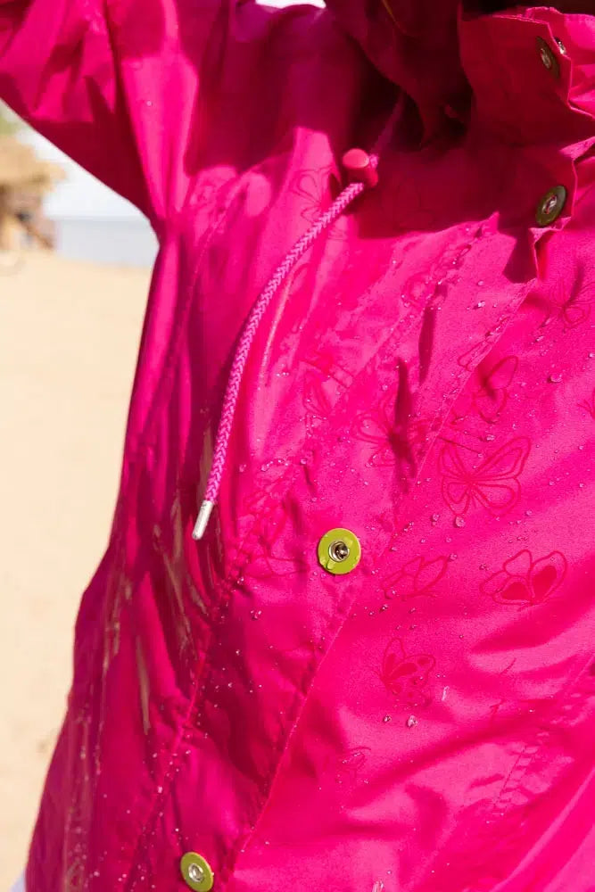 Close-up of a pink raincoat with butterfly designs on a blurred beach background