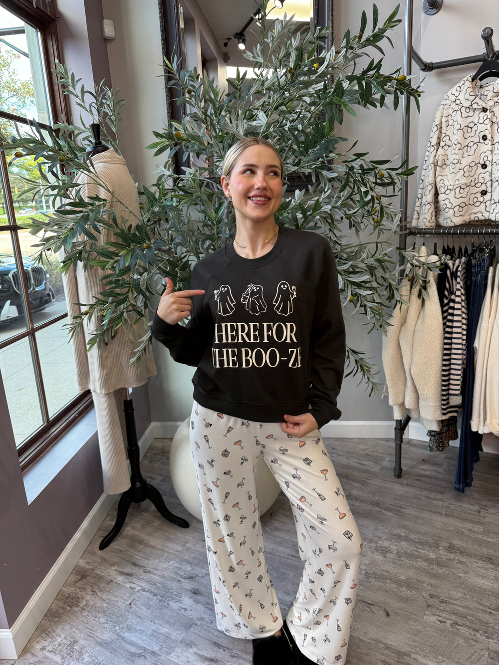 Here for the Boo-ze Sweatshirt in black with ghost graphic, front view styled with cocktail print pajama pants