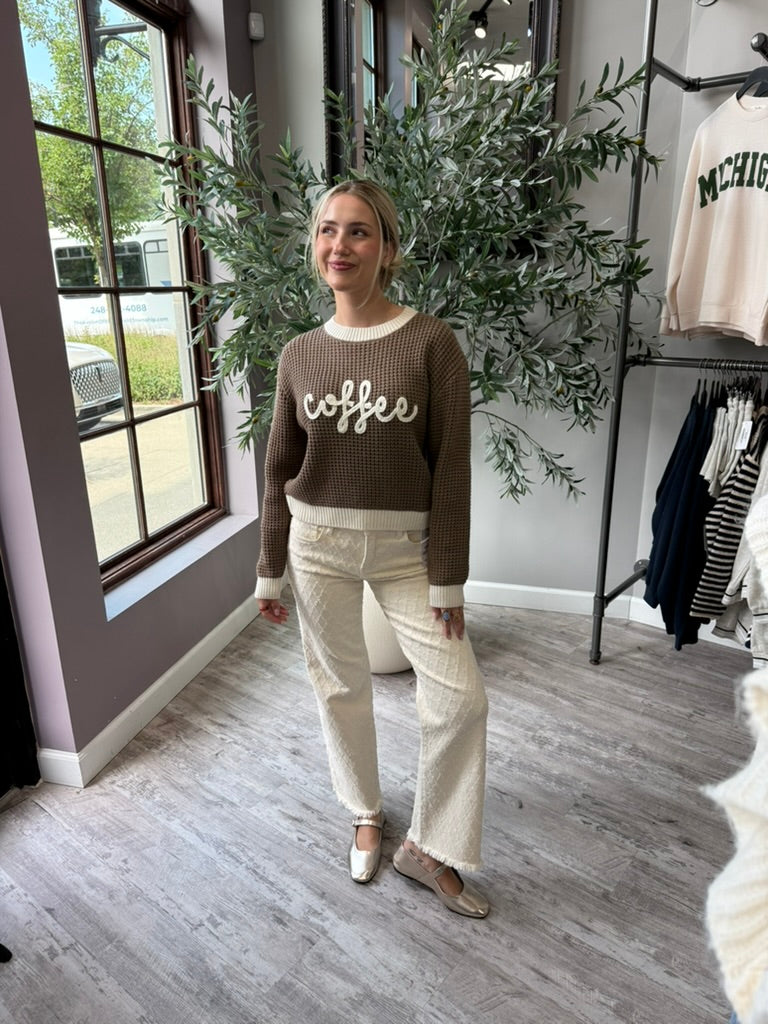 A woman stands in a boutique wearing a brown waffle-knit sweater with &