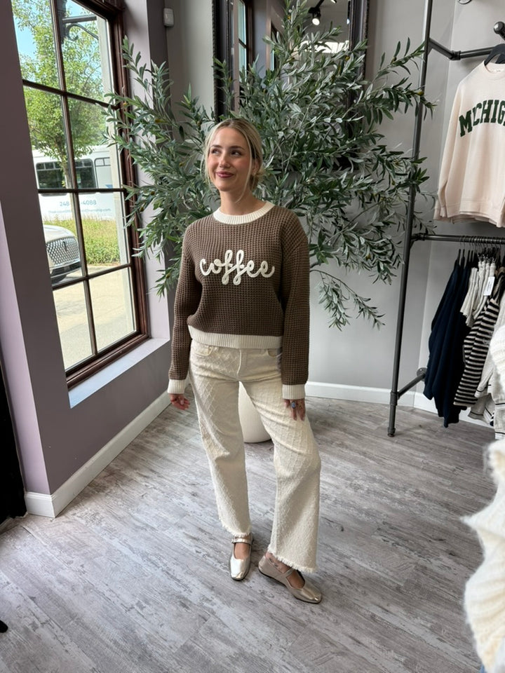 A woman stands in a boutique wearing a brown waffle-knit sweater with &