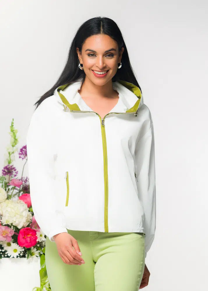 Woman wearing a white jacket with green accents standing next to flowers on a white background