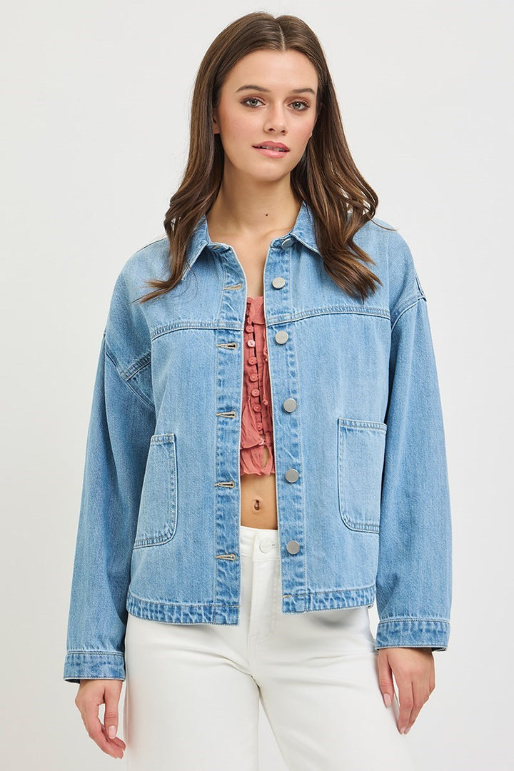 Woman wearing a light blue denim jacket over a pink top on a white background