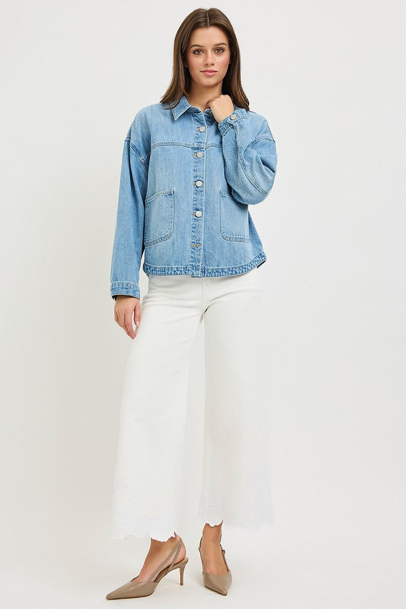 Woman wearing a light blue denim jacket and white pants on a plain background