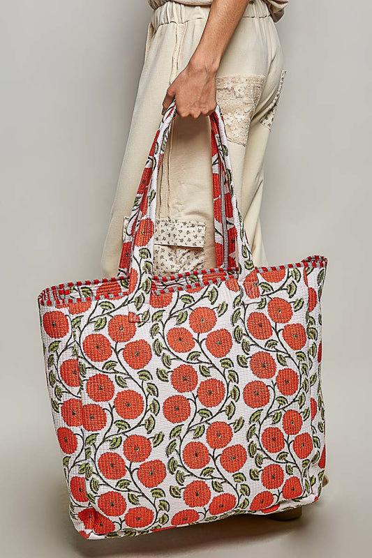 Person holding a tote bag with red floral pattern on a plain background