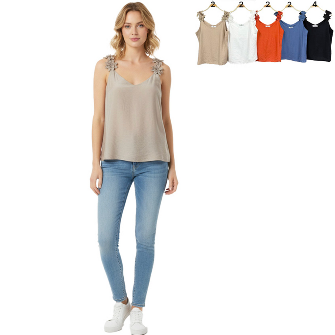 Woman wearing a beige tank top with floral embellishments and light blue jeans, standing next to a row of color-swapped tank tops on hangers.