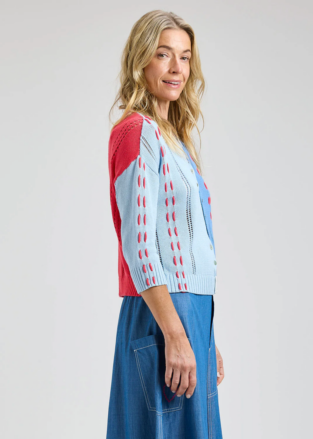 Woman wearing a colorful cardigan and blue pants on a plain background