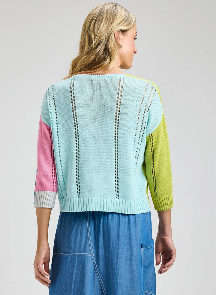 Woman wearing a colorful sweater with a light blue, pink, and green design on a plain background