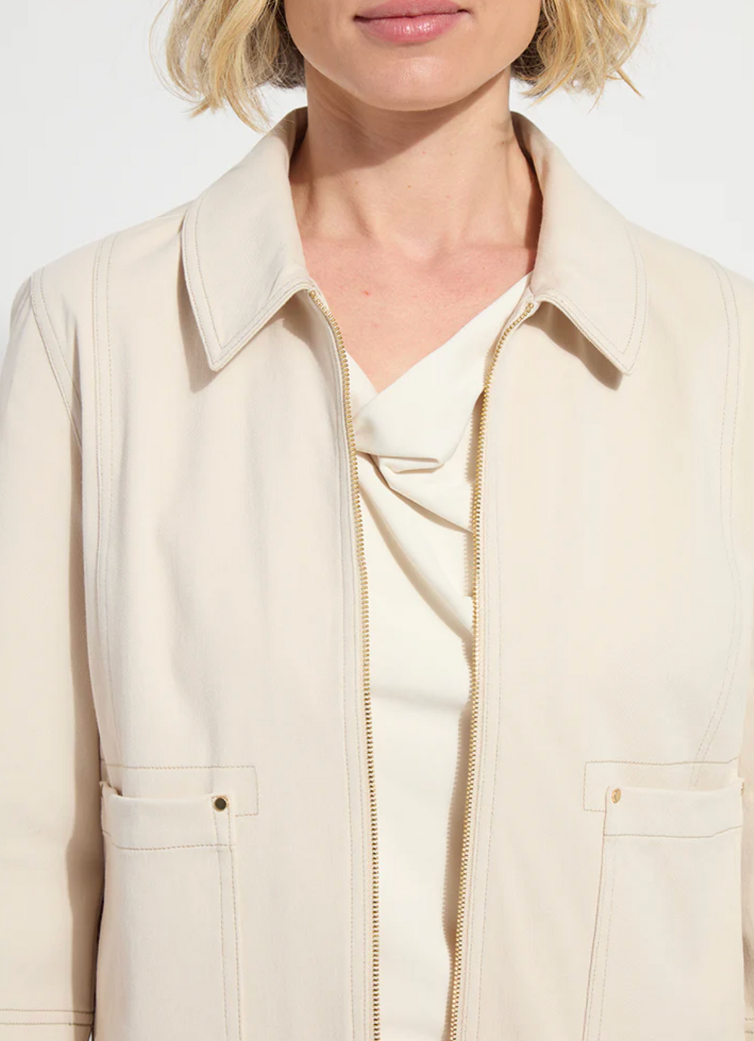 Close-up of a person wearing a beige jacket with a white shirt underneath.