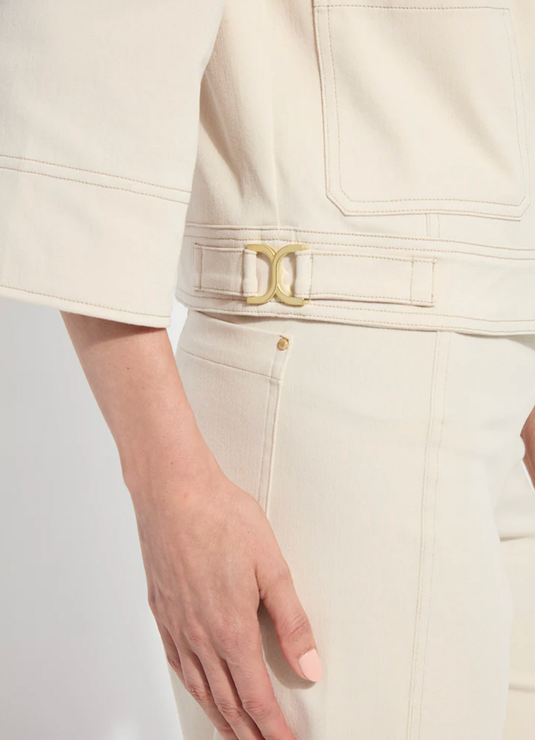 Close-up of a beige outfit with a gold belt buckle on a plain background
