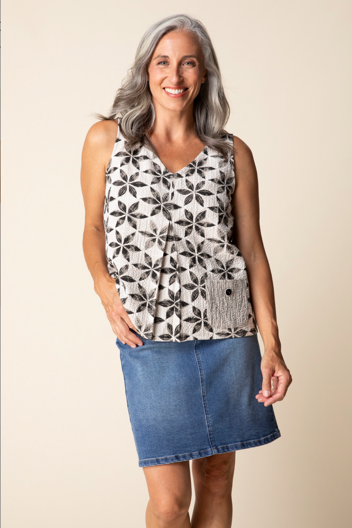 Woman wearing a sleeveless patterned top and denim skirt on a beige background