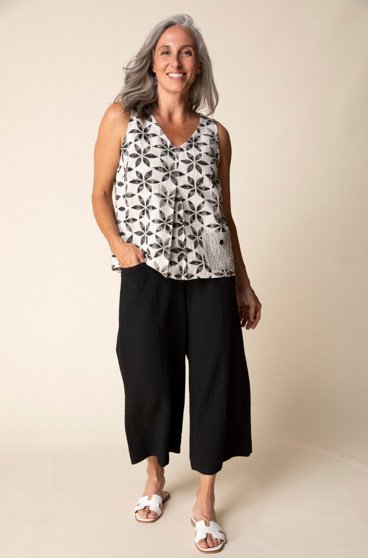 Woman wearing a sleeveless patterned top and black wide-leg pants against a beige background