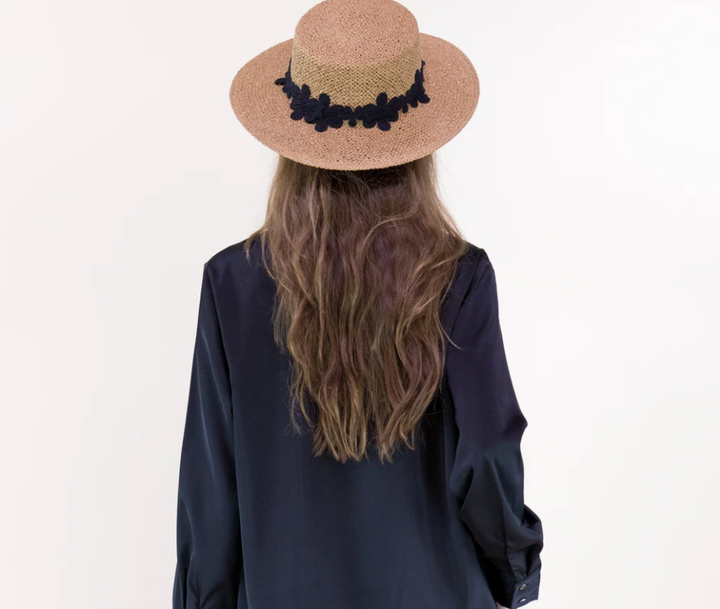 Person wearing a straw hat with black embellishments on a plain background