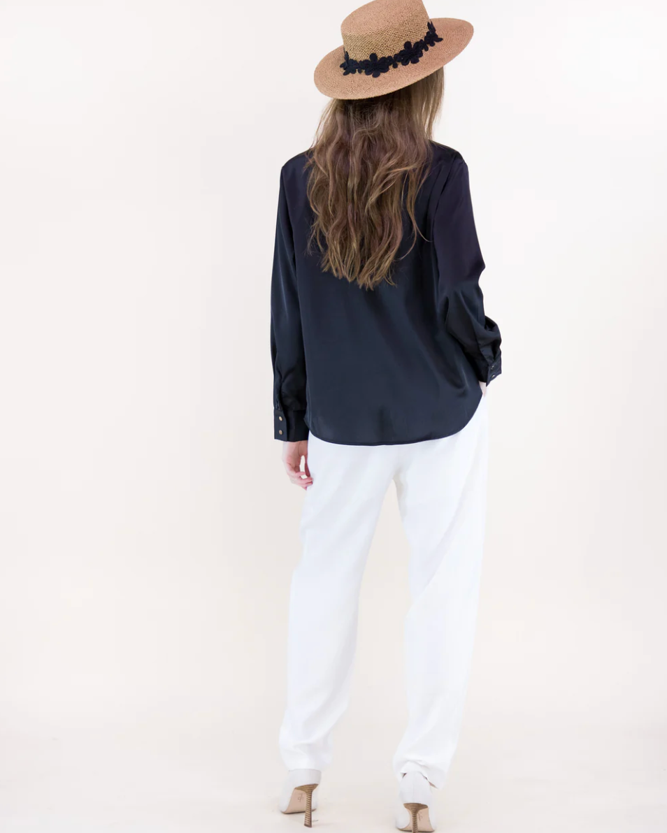 Person wearing a navy blue top and white pants with a beige hat on a plain background