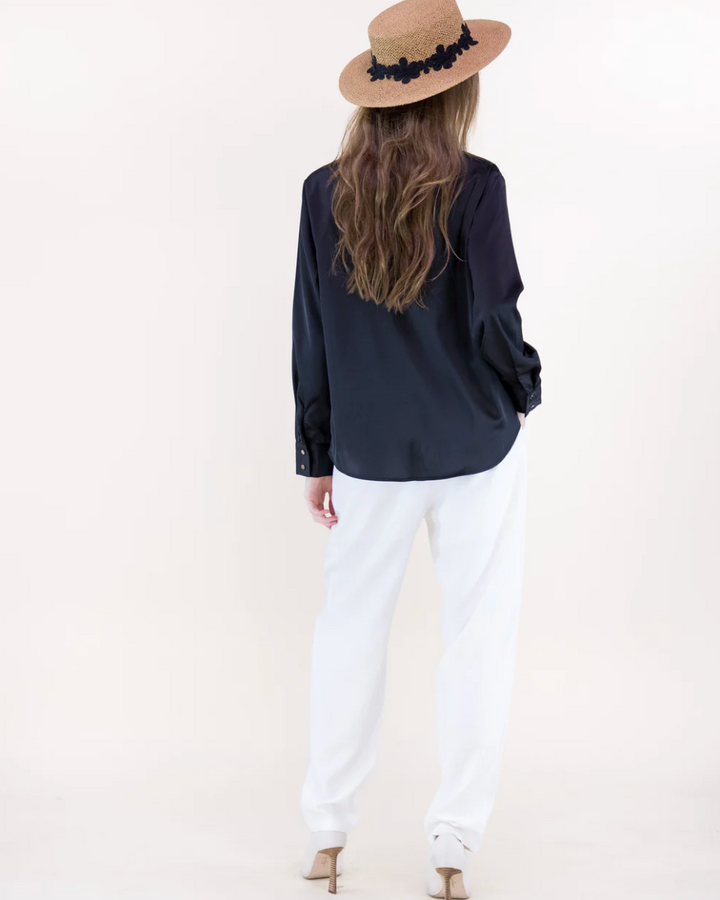 Person wearing a navy blue top and white pants with a beige hat on a plain background